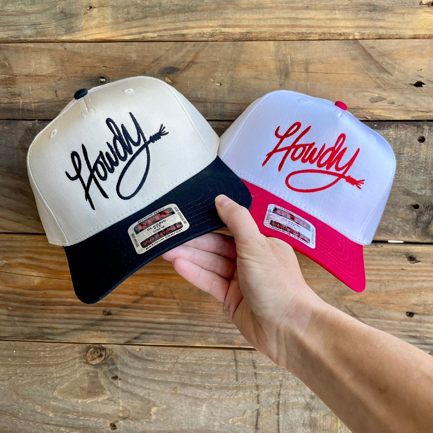 Two baseball caps with 'Howdy' embroidered text on a wooden surface