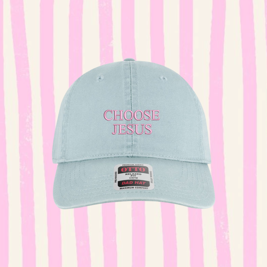 A light blue baseball cap with 'CHOOSE JESUS' embroidered in pink on the front, set against a pink and cream vertical striped background.