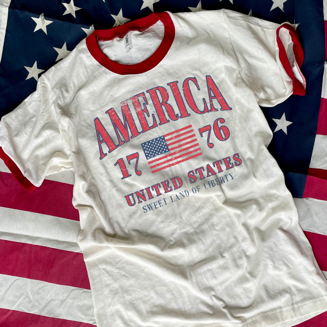 White t-shirt with 'America 1776' text and American flag on a background of the American flag.