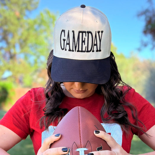 Person wearing a 'GAMEDAY' cap holding a football outdoors