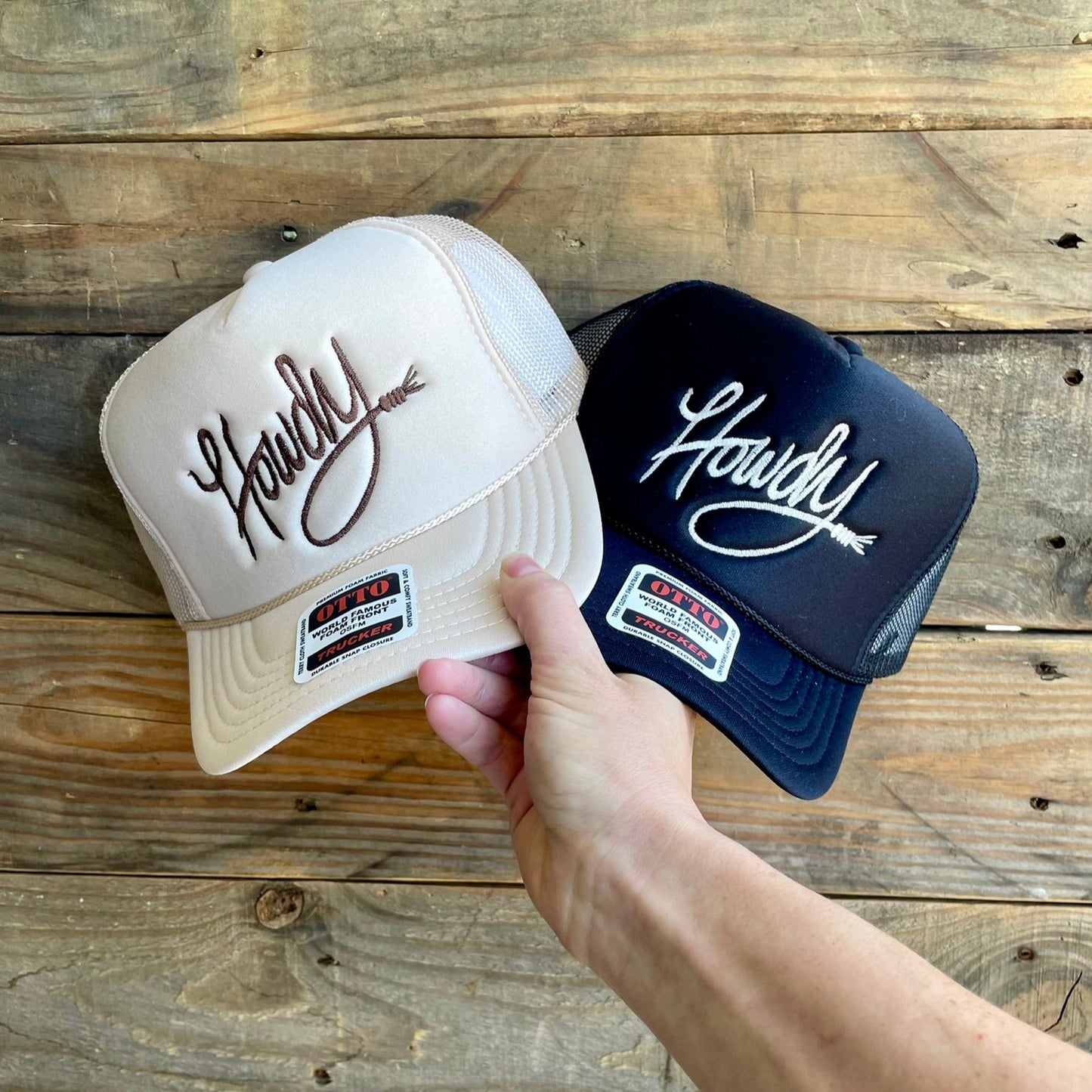Two hats, one beige and one black, with 'Howdy' text on a wooden surface.