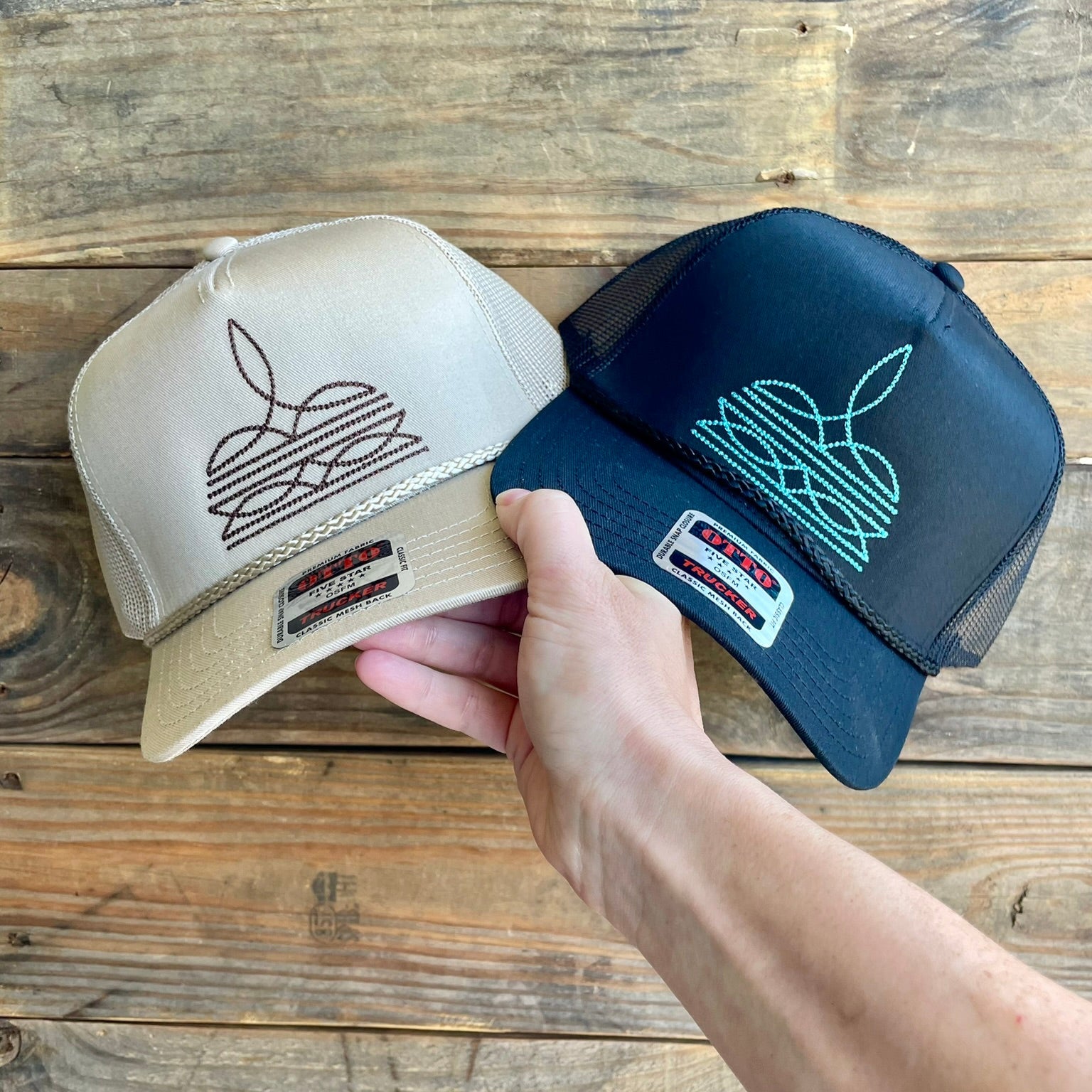 Two hats, one beige and one black, held by a hand on a wooden surface.