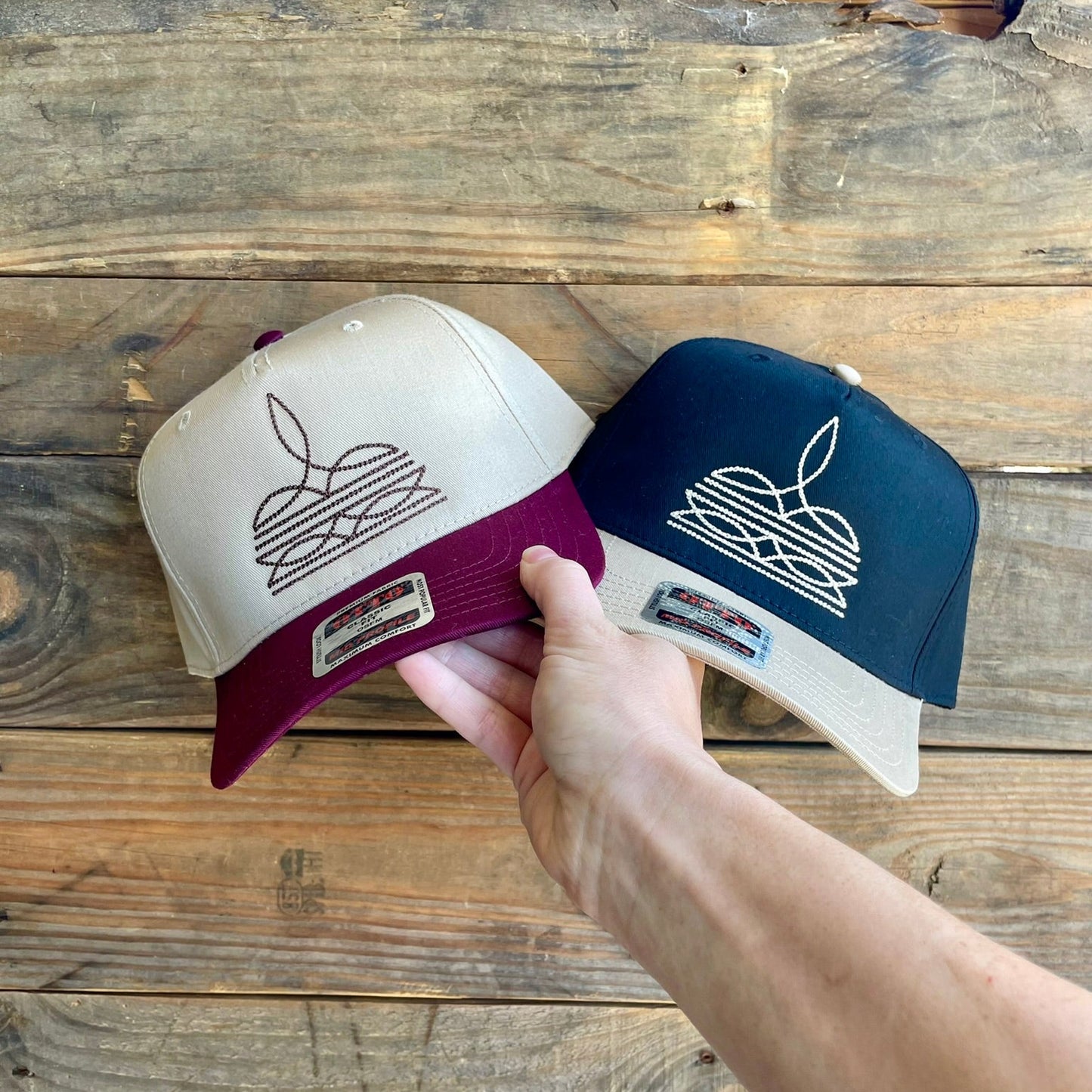 Two baseball caps with embroidered designs on a wooden surface
