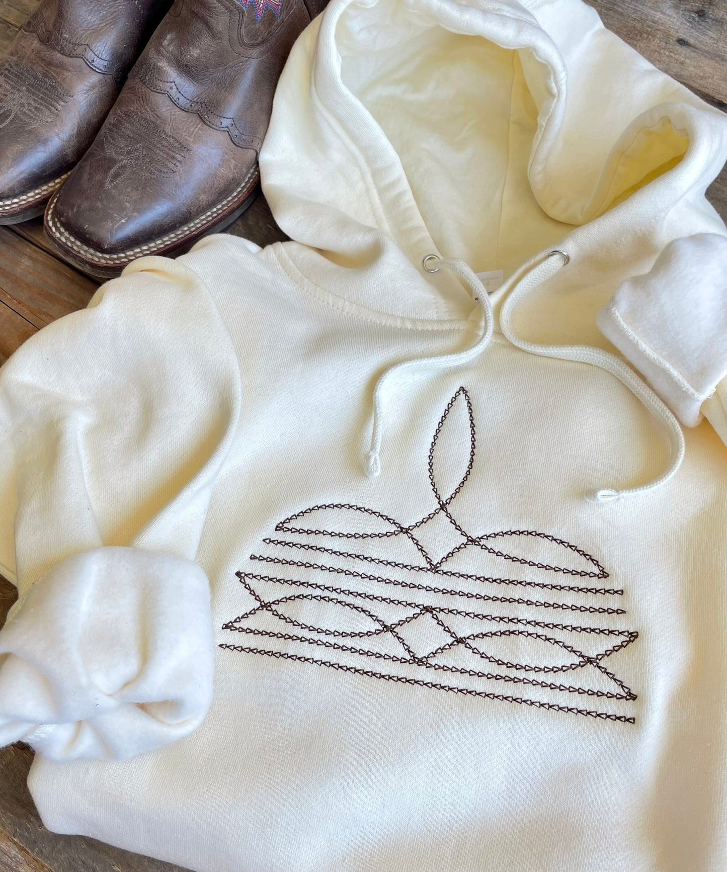Cream hoodie with a brown boot stitch design on a wooden surface
