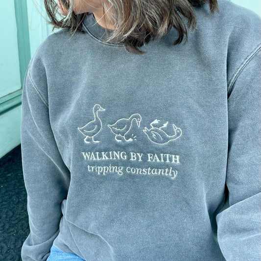 faded black crewneck embroidered with 3 geese and phrase "Walking by Faith tripping constantly"